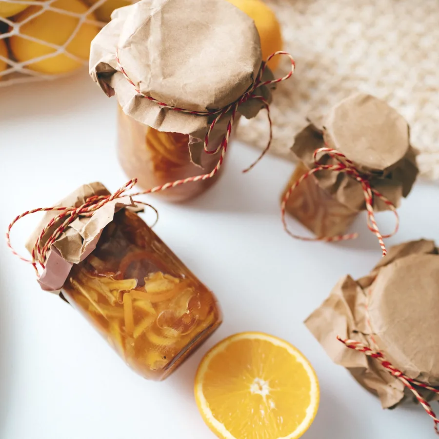 Preserve jars with kraft-paper caps tied in twine, beside a halved orange.