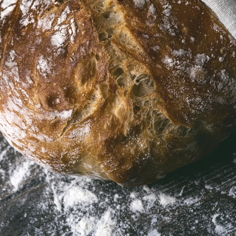A fresh sourdough loaf wrapped in linen, dusted with flour.